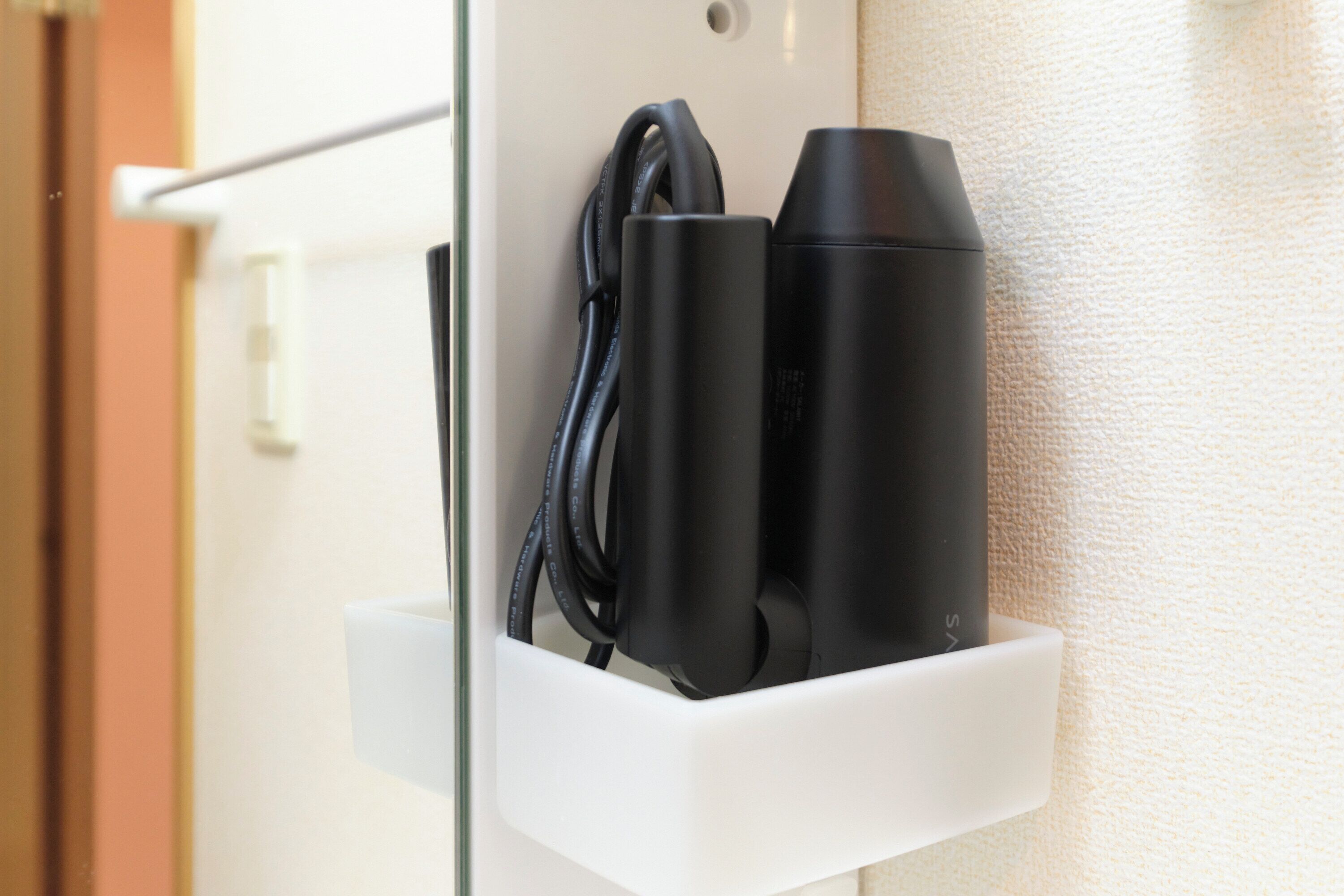 A white wall-mounted charging station with a black cable and two black cylindrical devices.
