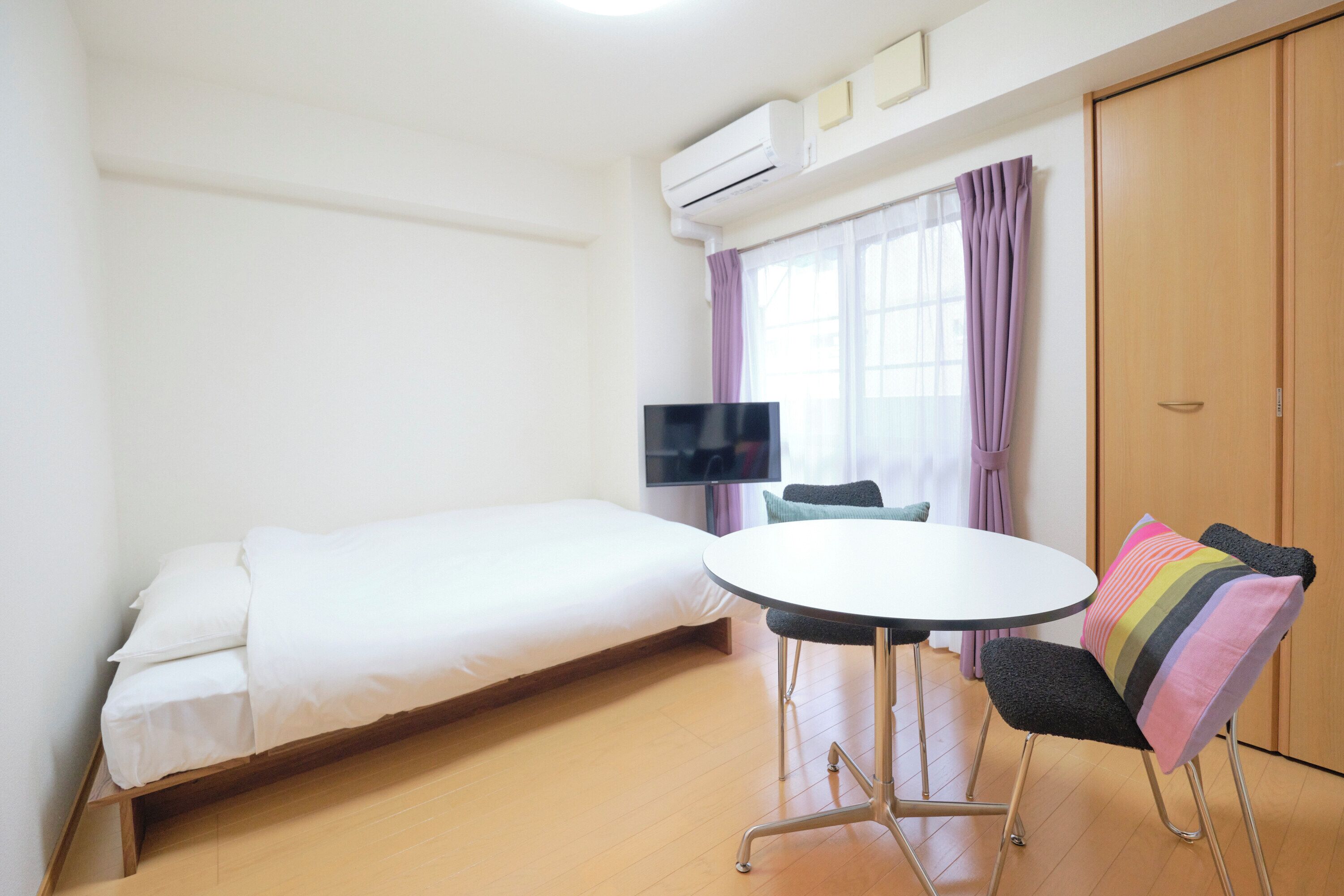 A room with a bed, a round table, a chair, a TV, and a wardrobe.
