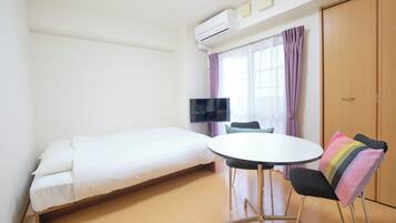 A room with a bed, a round table, a chair, a TV, and a wardrobe.