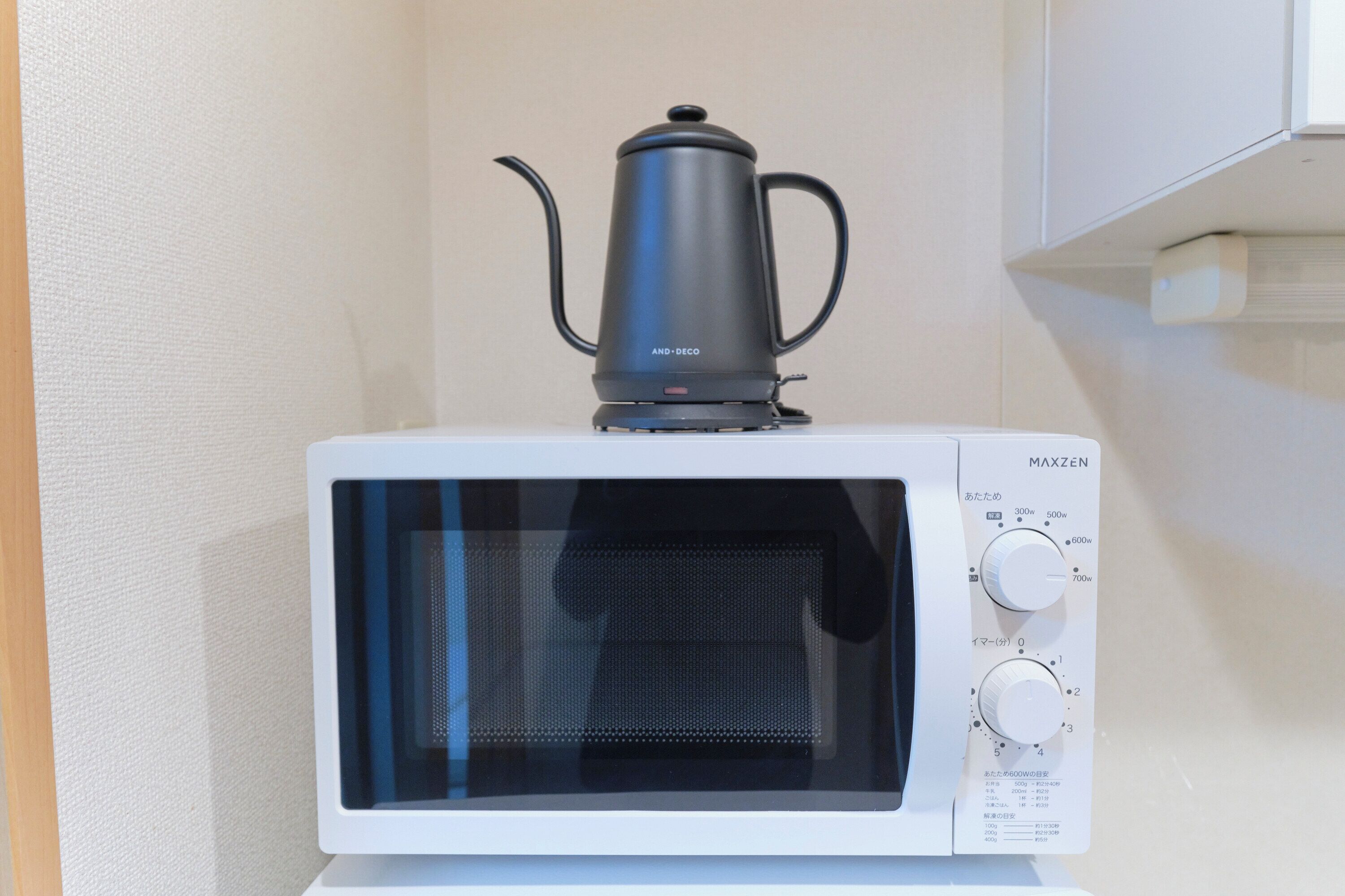 A white microwave oven with a black coffee pot on top, a control panel with various settings, and a white cabinet in the background.