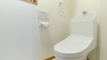 A small, white bathroom with a toilet, a wall-mounted flush handle, and a toilet paper holder.