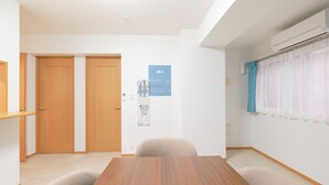 Una habitación con una mesa de madera, dos puertas, un aire acondicionado instalado en la pared y una ventana con cortina azul.