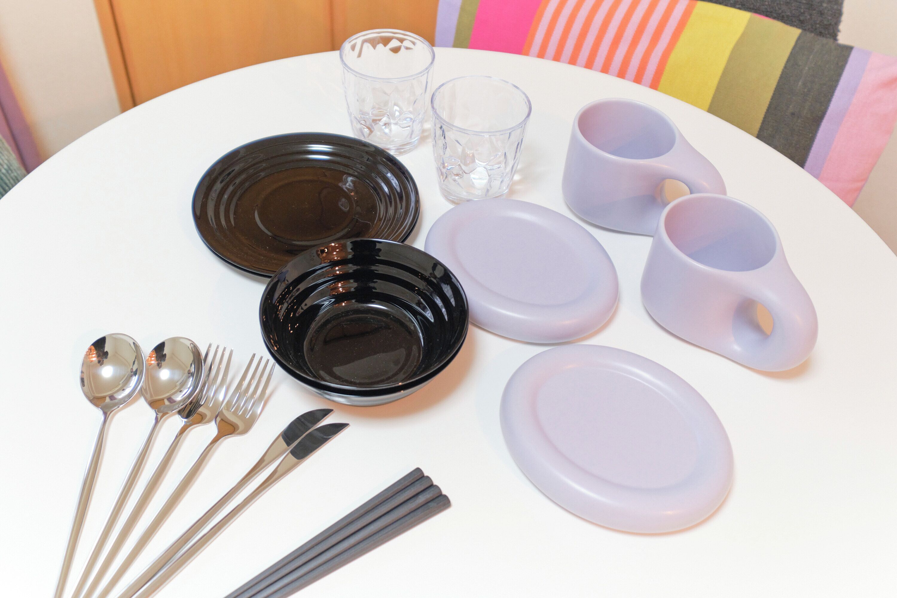 A dining set with plates, bowls, cutlery, and glasses on a white table.