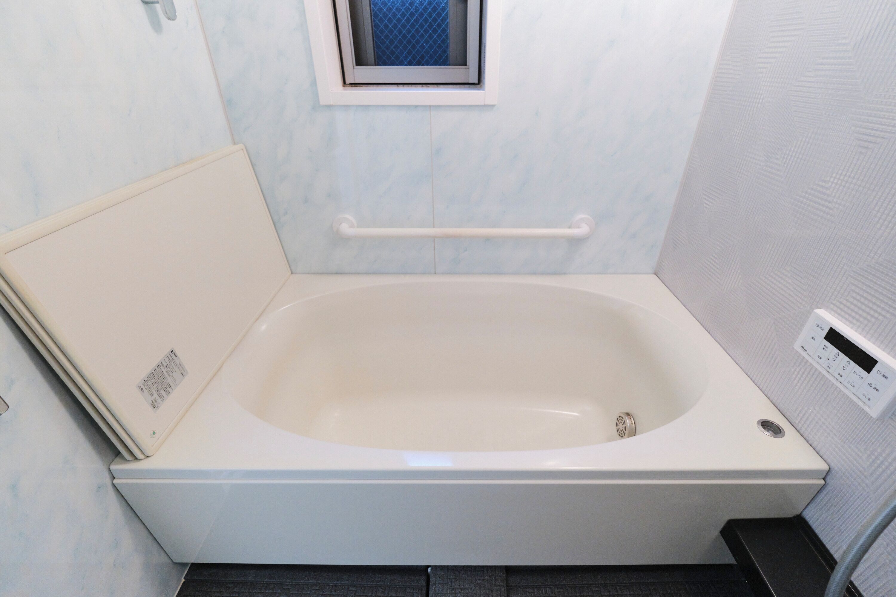 Bagno con una vasca da bagno bianca, una piccola finestra, un mancorrente e un pannello di controllo.