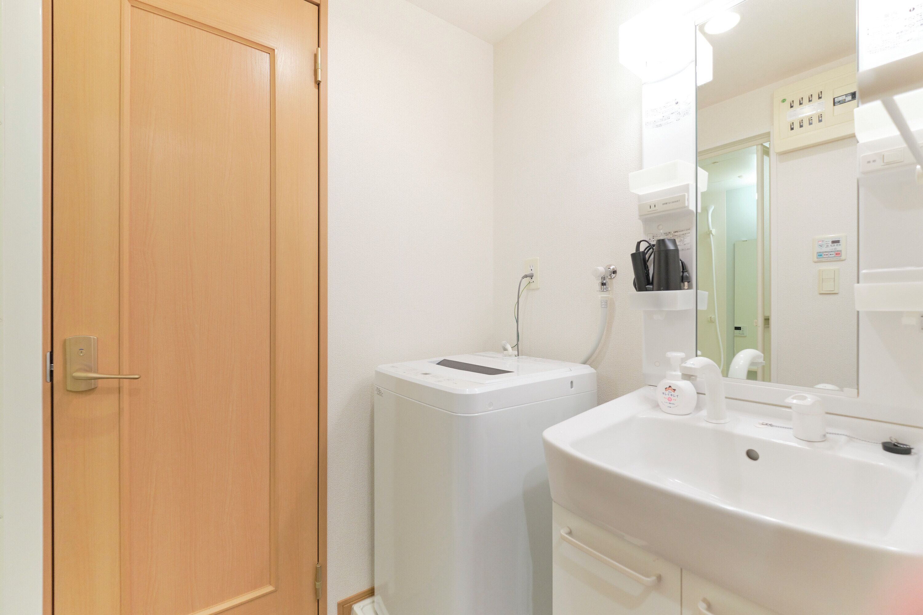 Un bagno con una porta in legno, una lavatrice bianca, un lavandino con uno specchio e un interruttore sulla parete.