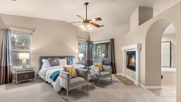 A spacious bedroom with a large bed, two armchairs, a ceiling fan, and a fireplace. - BNEW 6BR Postmodern 3k+sqft. Home in ABQ w/ Pool! (Albuquerque)