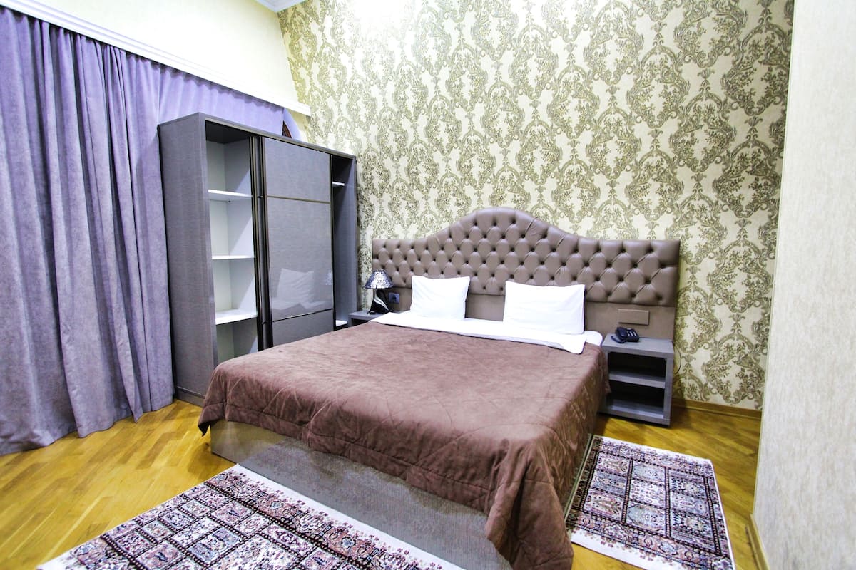 A bedroom with a large bed, a wardrobe, a nightstand, and a patterned rug.
