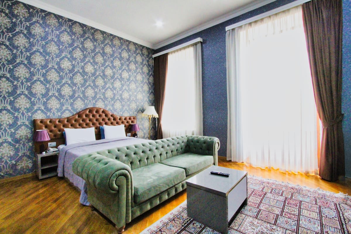 A bedroom with a green sofa, a wooden headboard, a bedside table, and a patterned rug.
