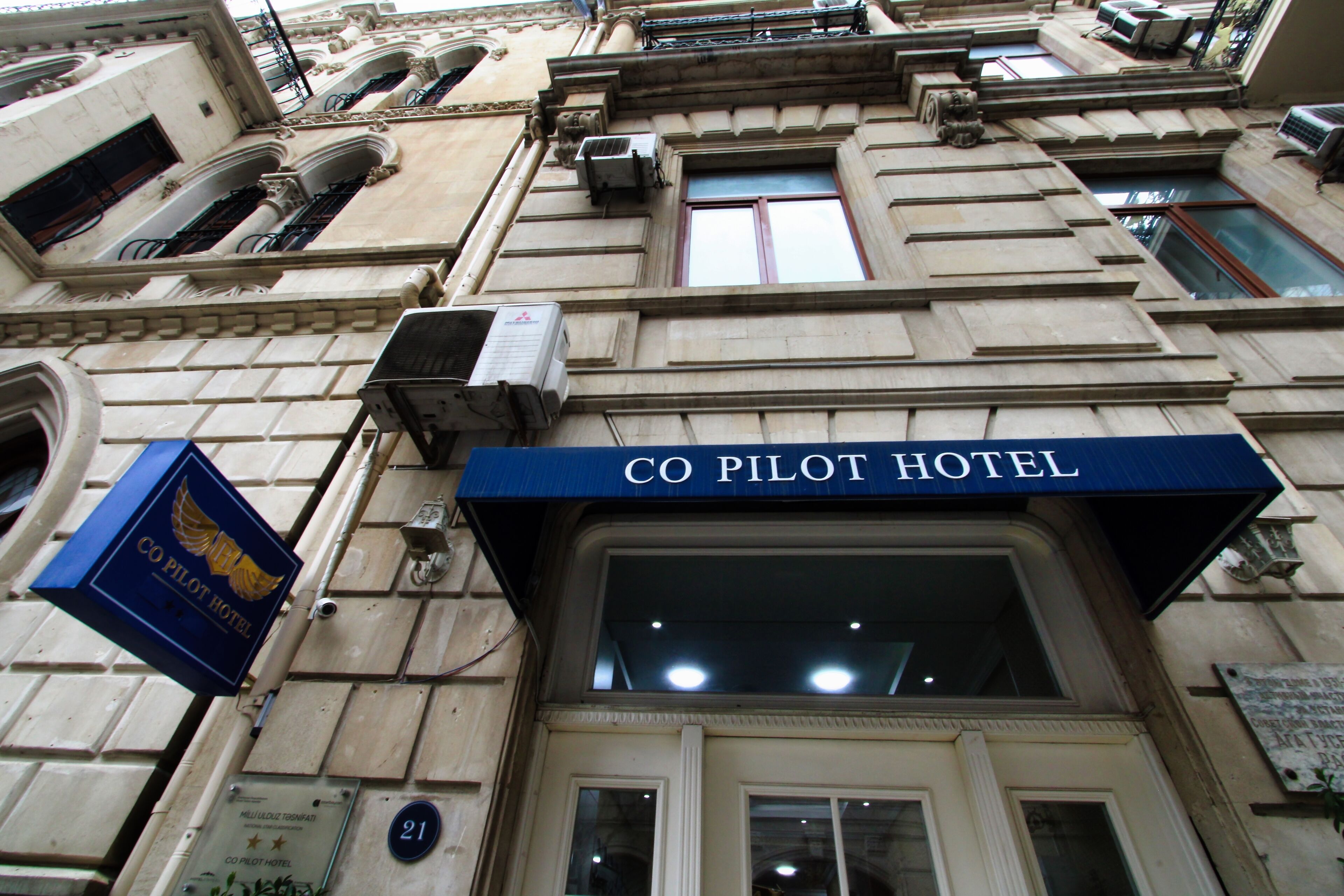 The facade of the Co Pilot Hotel with a prominent sign, a number plaque, and air conditioning units.