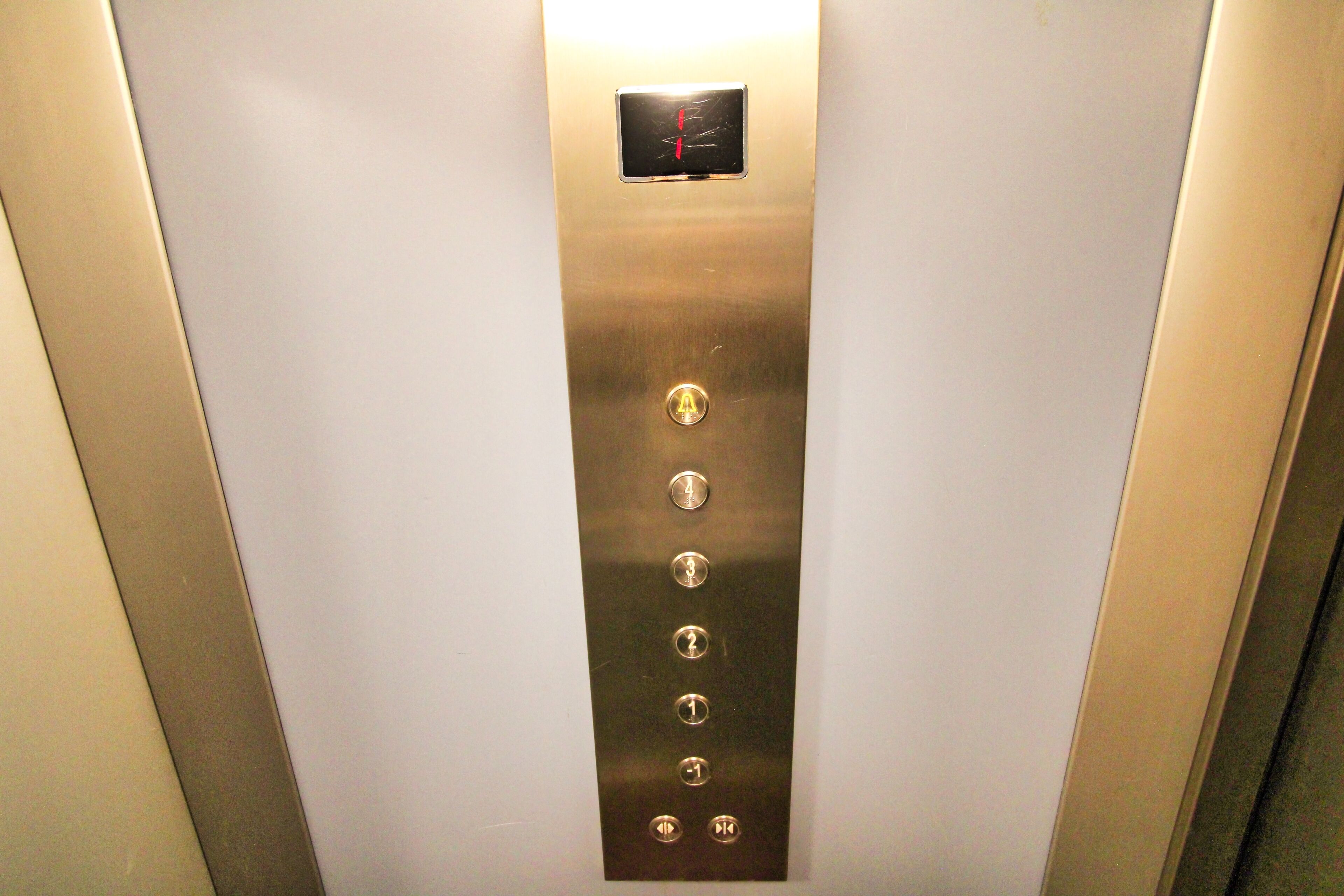An elevator interior with a metallic panel featuring a red emergency button and five buttons labeled 1 to 5.