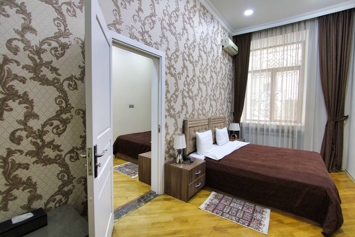 A hotel room with a large bed, a bedside table with a lamp, a wardrobe, and a mirror.