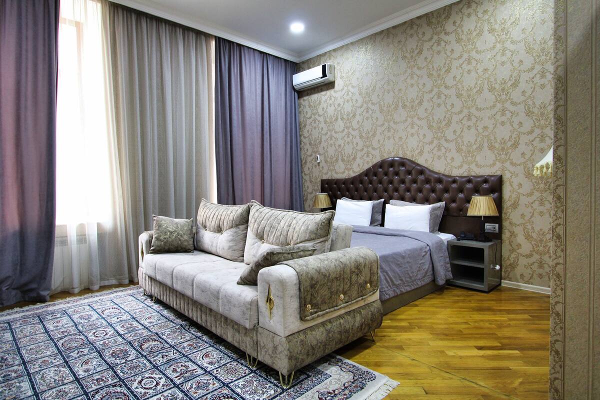 A bedroom with a sofa, a bed, a nightstand, and a patterned rug.