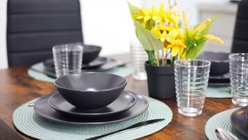 A dining table set with black bowls, clear glasses, and a potted yellow flower arrangement.