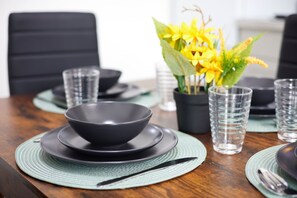 A dining table set with black bowls, clear glasses, and a potted yellow flower arrangement. - Ol-mumps Cosy 2bd Free Parking & Wifi (Oldham)