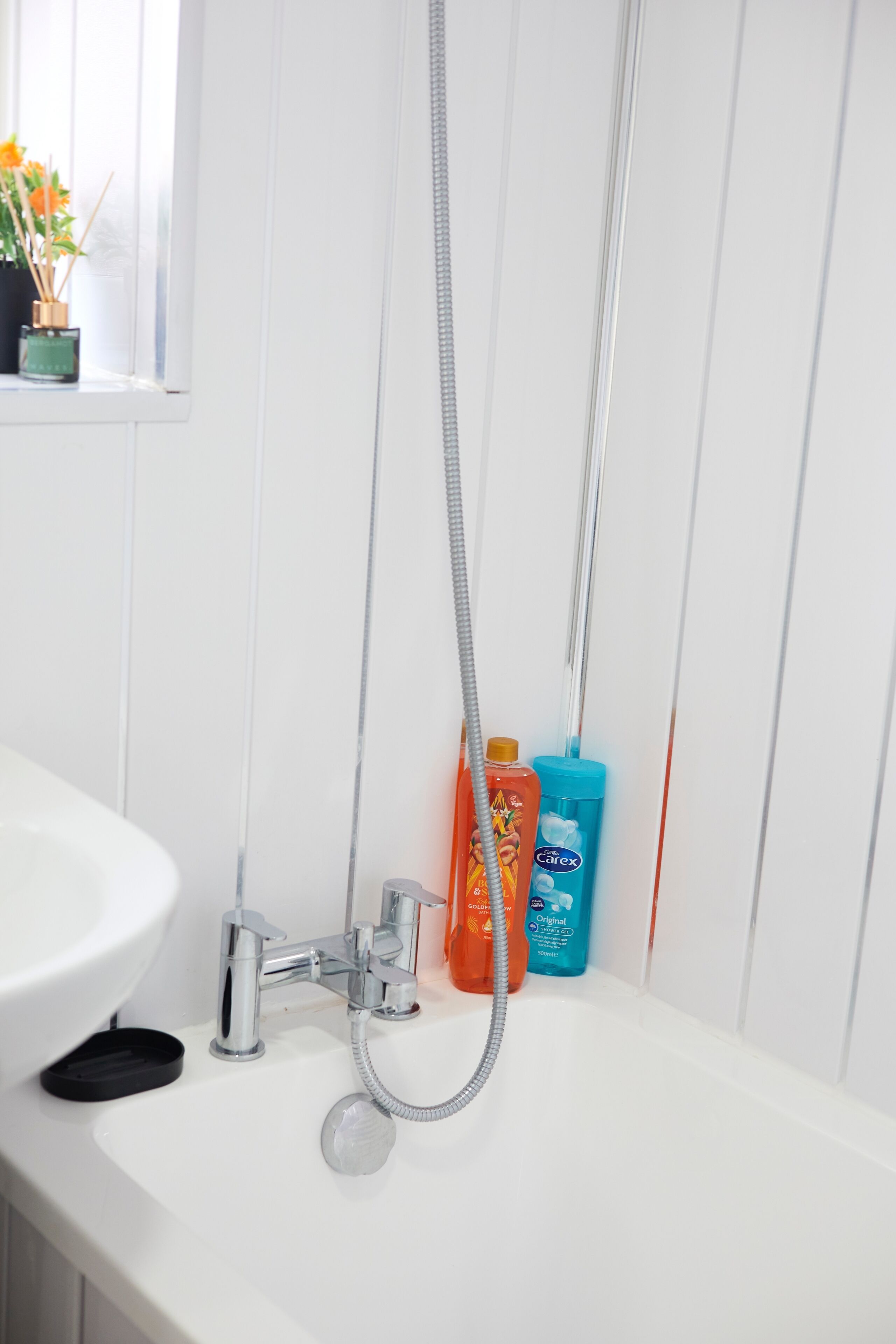 A bathroom with a white sink, a shower with a handheld showerhead, and two bottles of liquid soap.