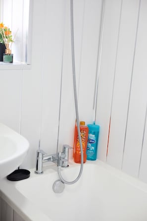 A bathroom with a white sink, a shower with a handheld showerhead, and two bottles of liquid soap. - Ol-mumps Cosy 2bd Free Parking & Wifi (Oldham)