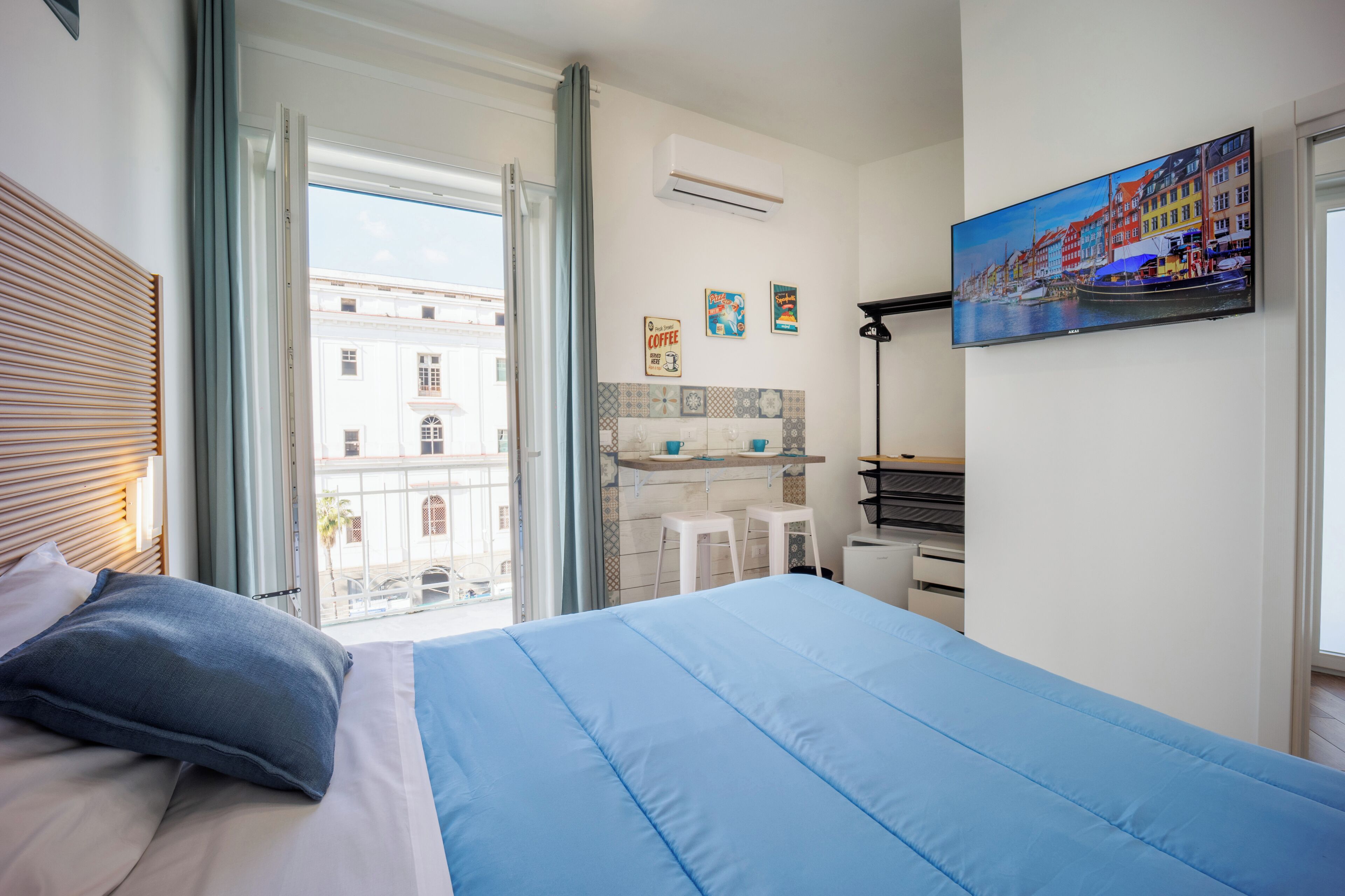 A bedroom with a large bed, a desk, and a view of buildings through a window.