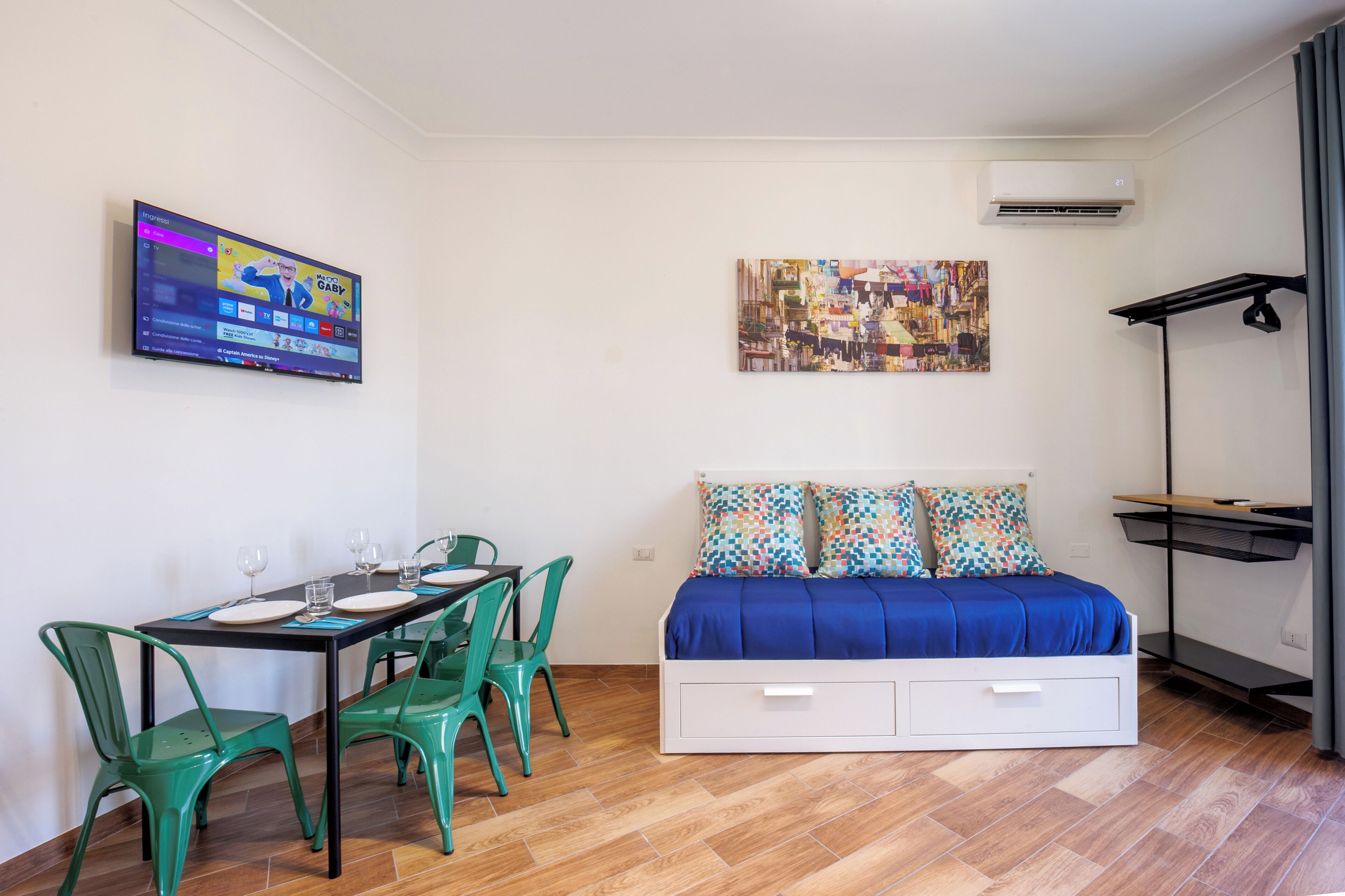 A modern room with a bed, a dining table with chairs, a TV, and a painting on the wall.