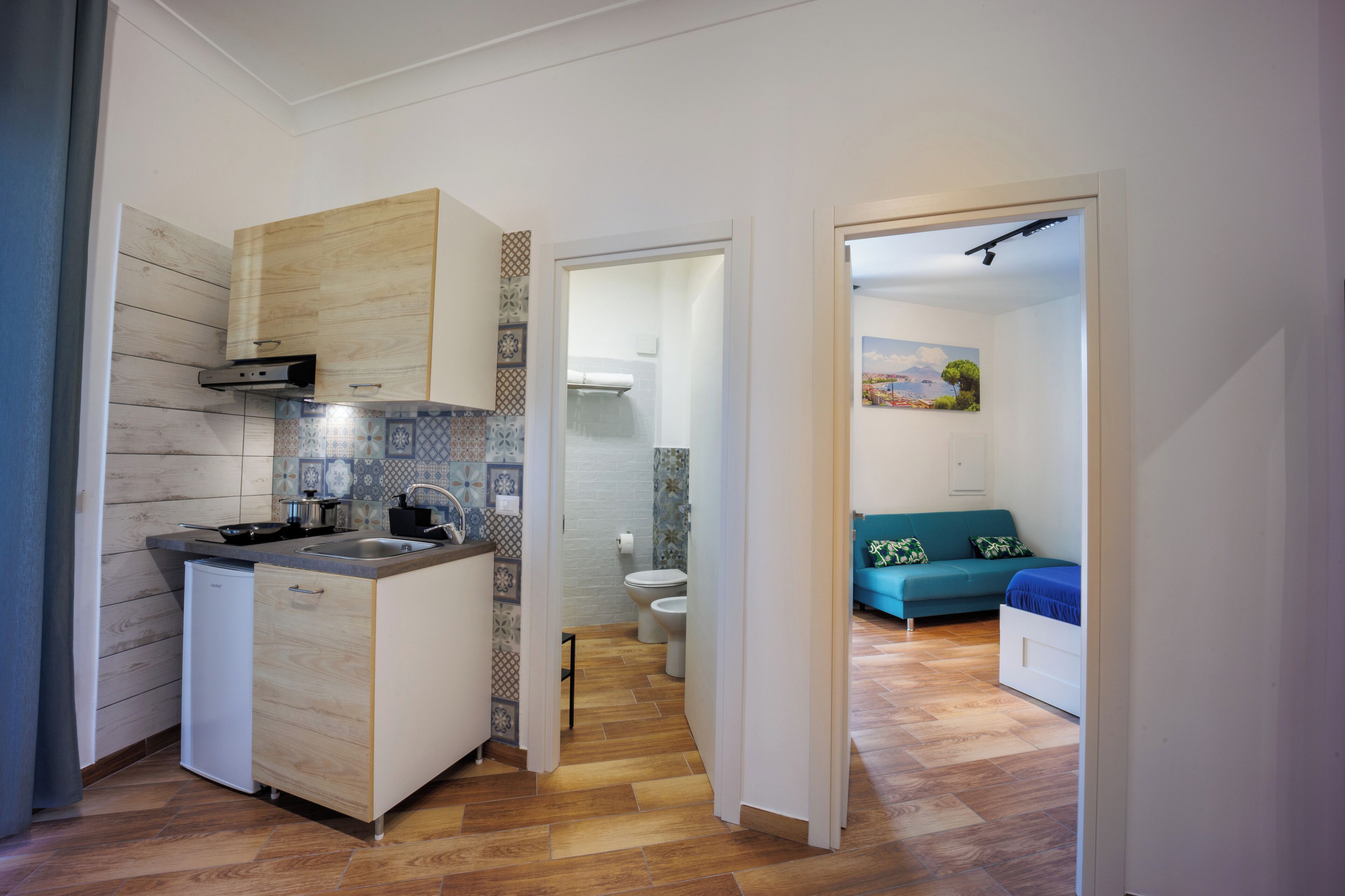 A compact kitchen with a dishwasher, a sink, and a stove. There is a small cabinet and a countertop with a toaster. The kitchen has wooden flooring and a tiled backsplash.