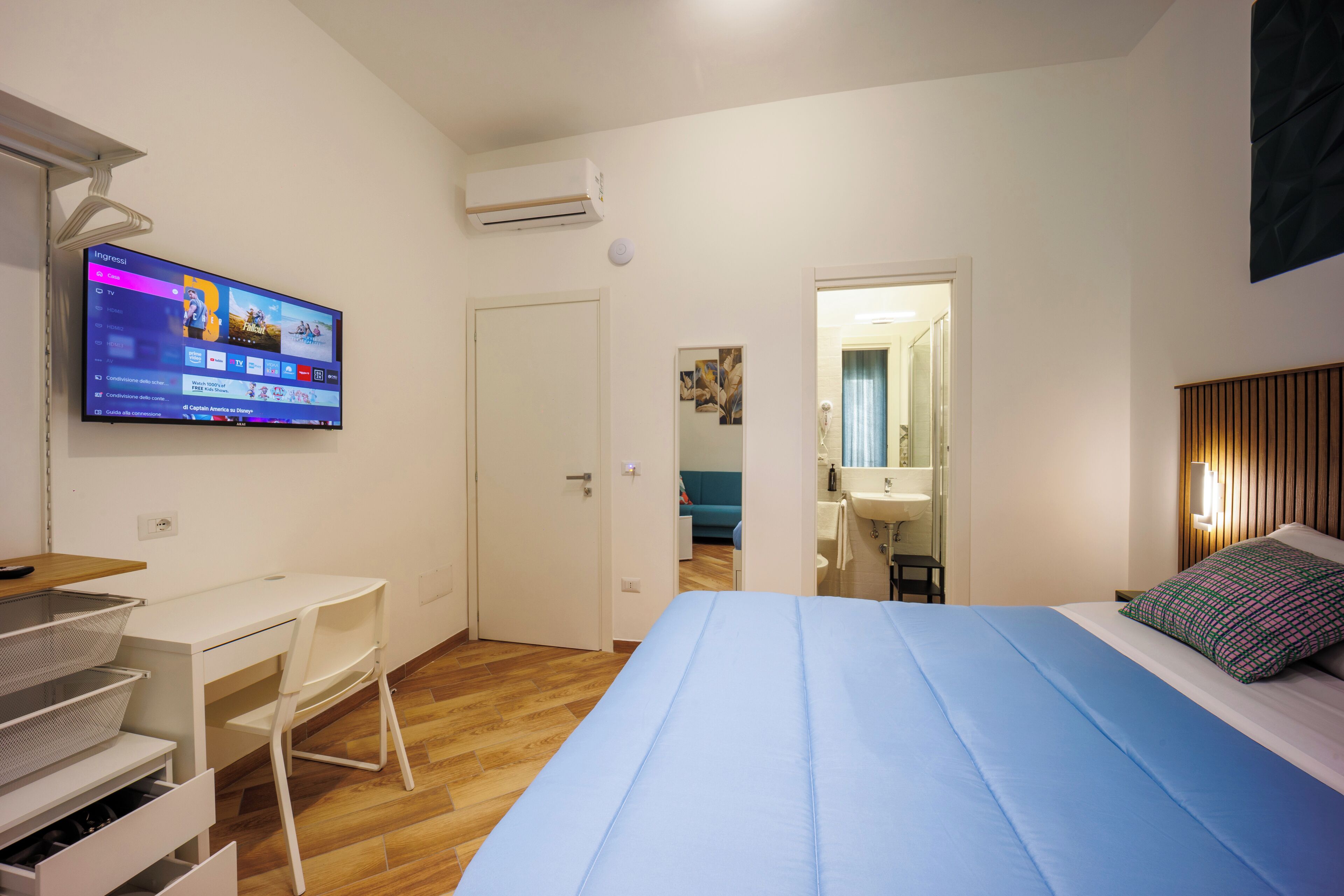 A bedroom with a bed, a desk, a chair, and a TV on the wall.