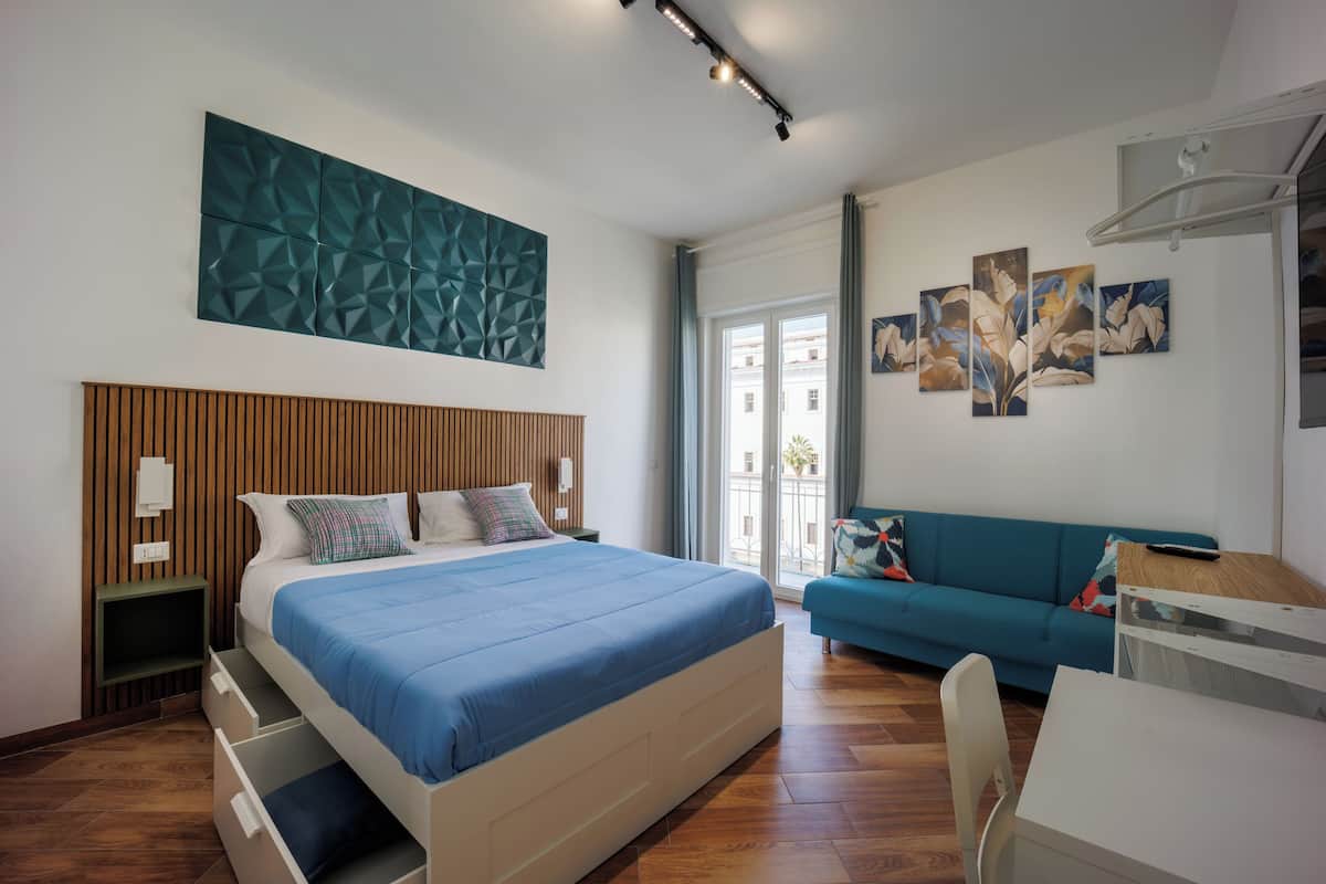 A modern bedroom with a large bed, a blue sofa, and a desk.