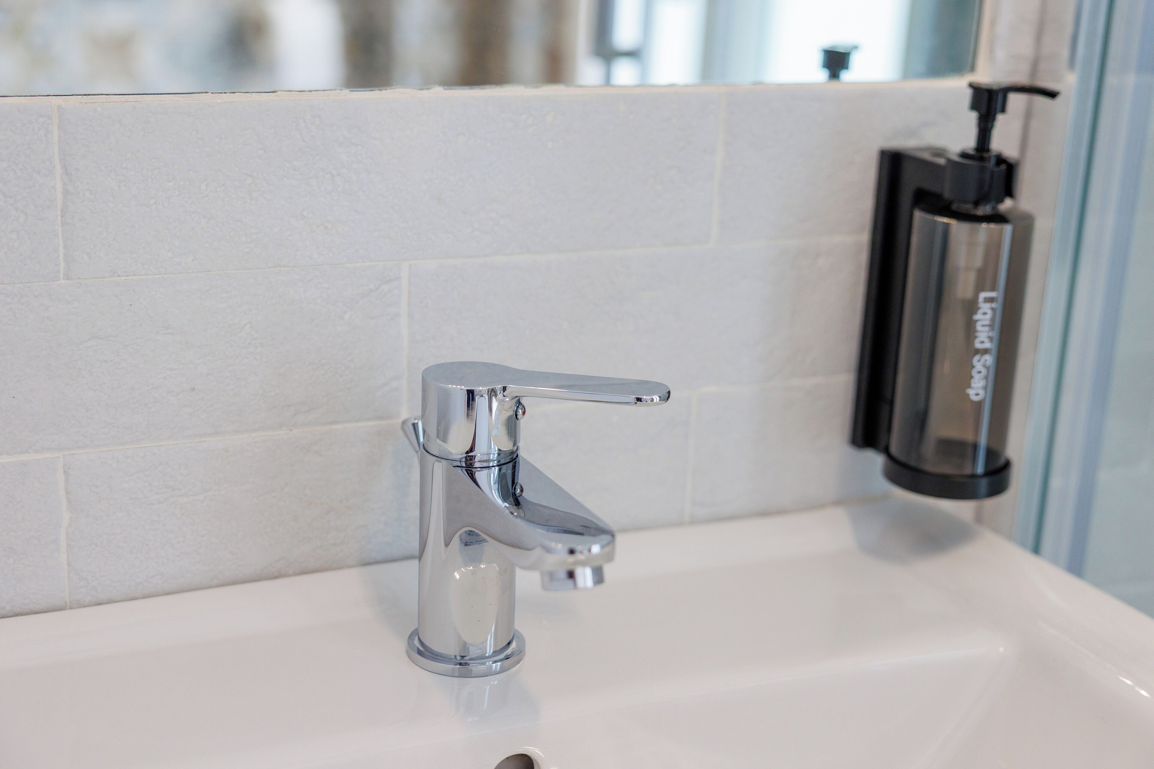 Une salle de bain moderne avec un robinet chromé, un distributeur de savon et des murs recouverts de carreaux blancs.