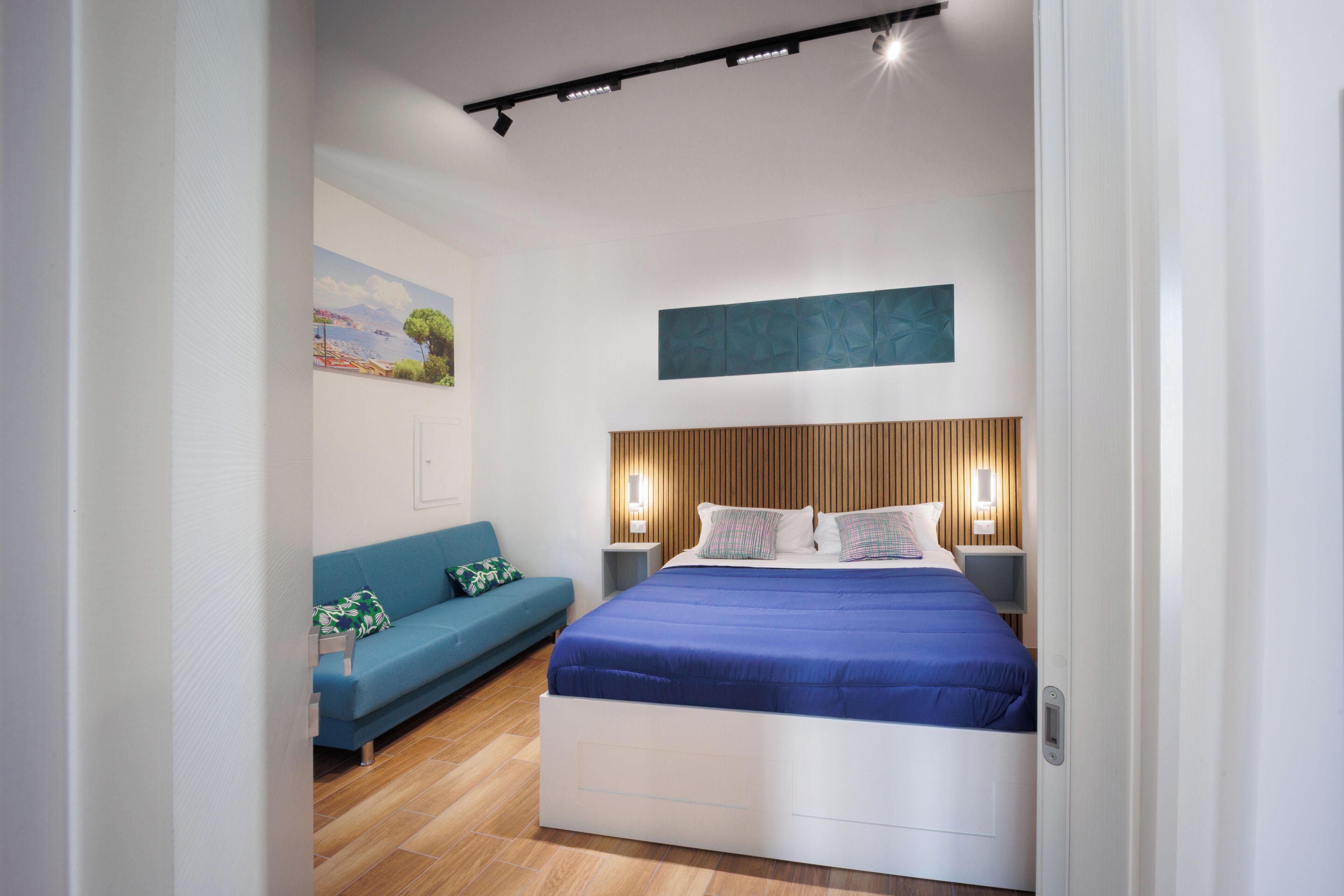 A modern bedroom with a bed, a blue sofa, and a painting on the wall.