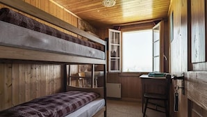 Dormitorio con literas, escritorio, silla, paredes de madera y una ventana.