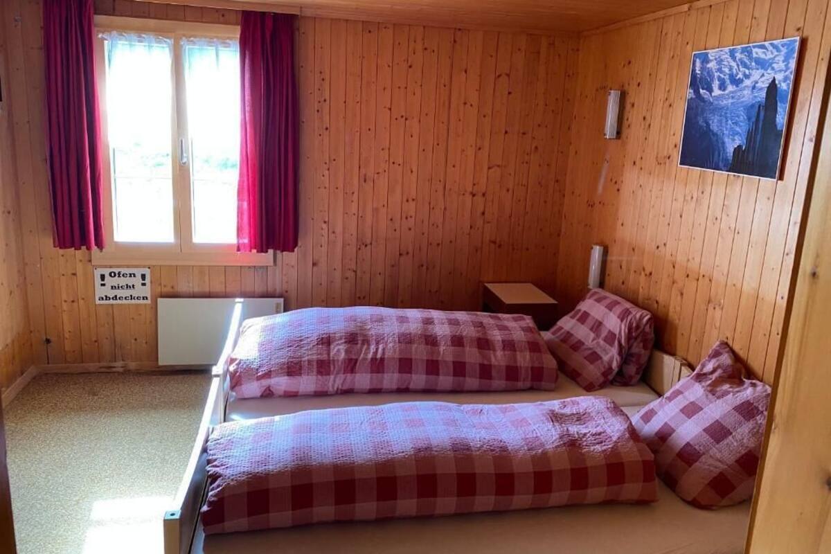 A wooden-paneled room with two beds, a nightstand, a radiator, and a window with curtains.