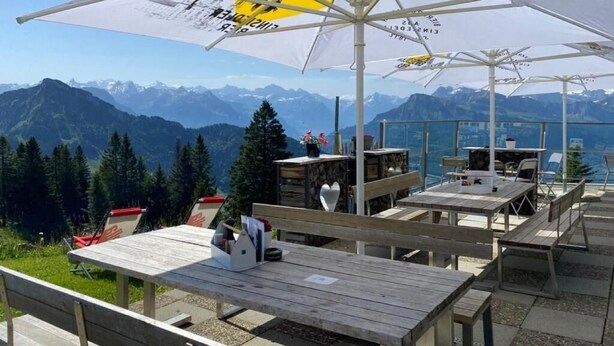 Un espacio al aire libre con mesas, bancos, sombrillas y vistas a montañas.