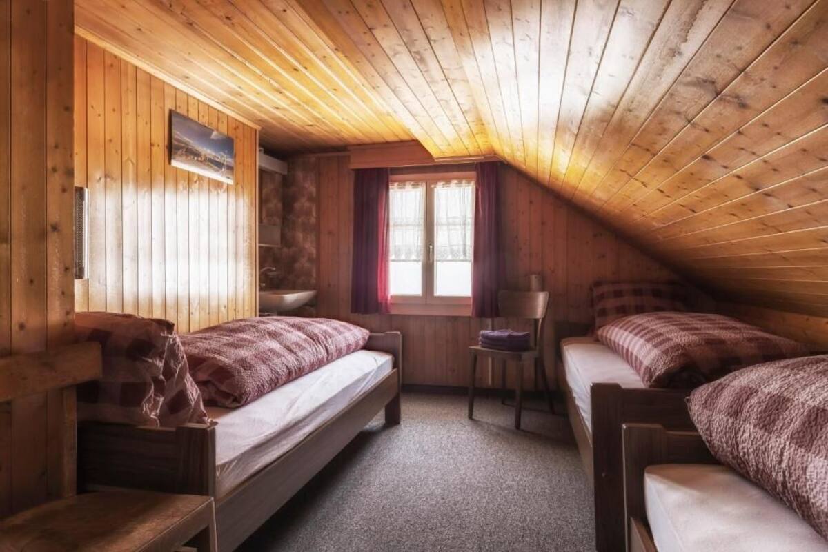 A cozy attic room with wooden walls and sloped ceilings, featuring two single beds and a chair.