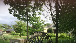 A water wheel in a grassy area with trees and buildings in the background. - TATATE's little house (Longué-Jumelles)