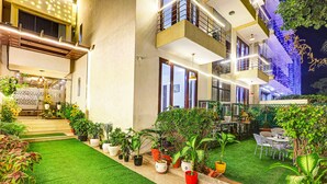 A hotel with a well-maintained garden, outdoor seating, and a balcony with a view. - Fabhotel B Stays (Gurugram)