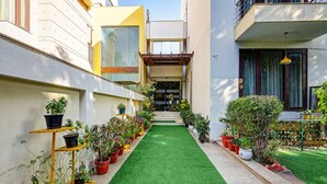 A narrow pathway with artificial green turf leading to a building entrance. - Fabhotel B Stays (Gurugram)