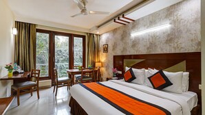 A hotel room with a bed, a desk, a chair, and a view of trees through the window. - Fabhotel B Stays (Gurugram)