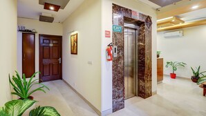 A hallway with an exit sign, a fire extinguisher, and an elevator. - Fabhotel B Stays (Gurugram)