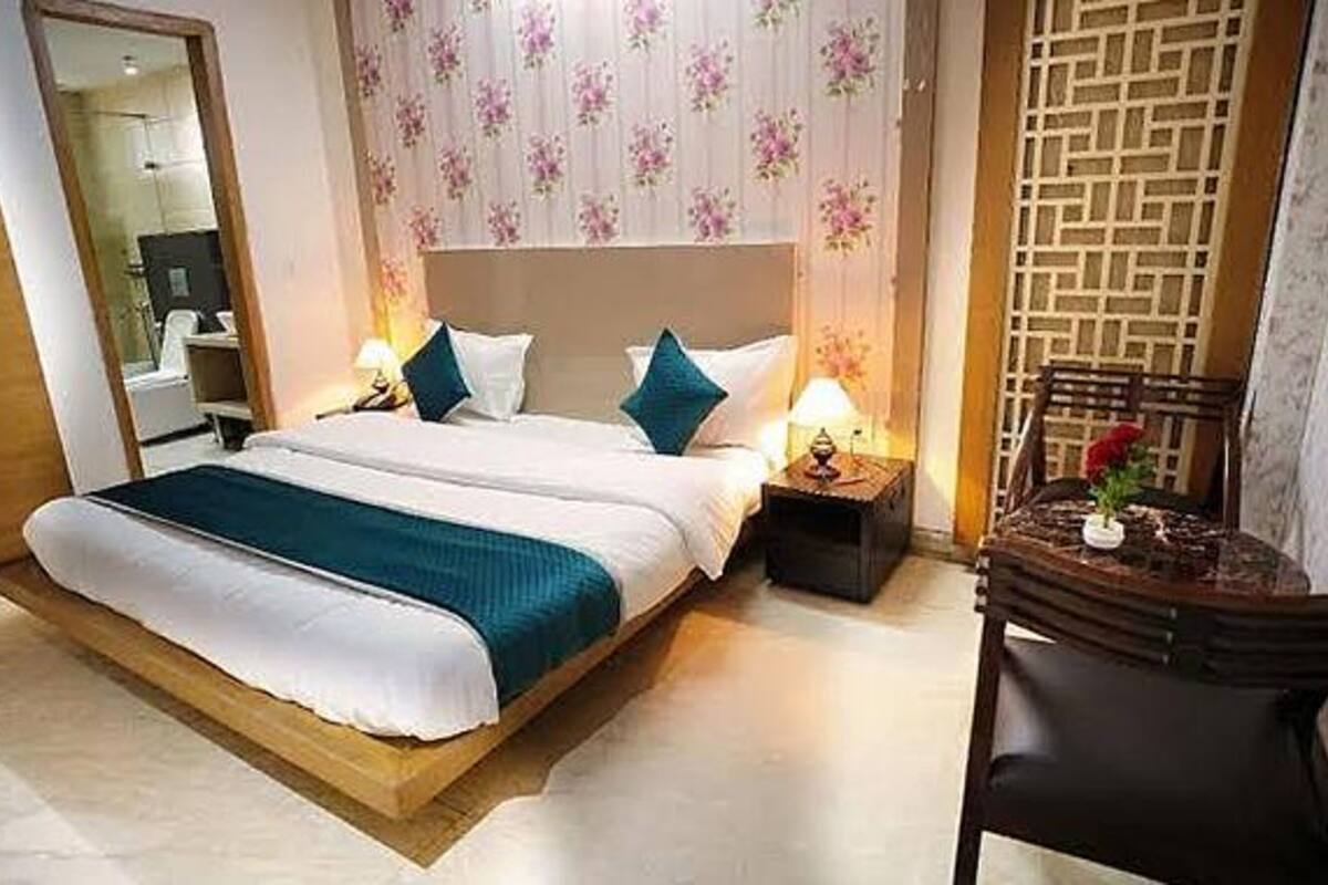 Habitación de hotel con una cama grande, dos mesitas de noche con lámparas, una silla de madera y un panel decorativo en la pared.