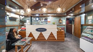 A reception area with a wooden reception desk, a glass table, and two people seated on a couch. - FabHotel I Residency - Koramangala (Nr St. John's Hospital) (Bengaluru)