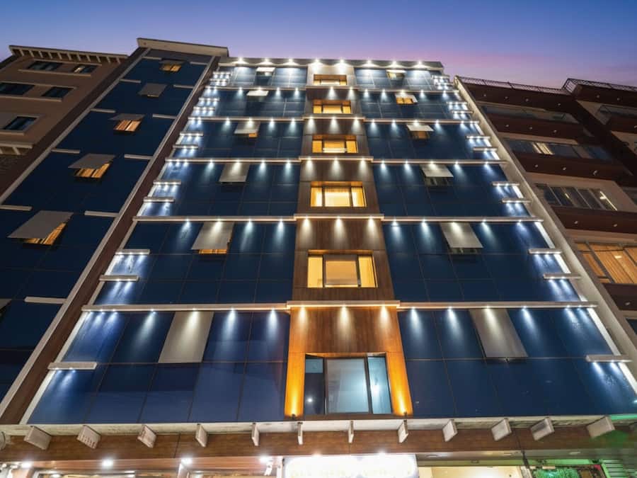 Un hotel de varios pisos con fachada moderna, que presenta una grilla de ventanas y paneles iluminados.