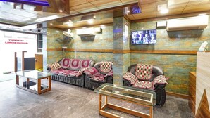 A reception area with leather sofas, a glass table, and a TV screen displaying a video. - FabHotel I Residency - Koramangala (Nr St. John's Hospital) (Bengaluru)
