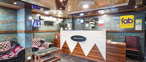 Zona de recepción de un hotel con un mostrador de madera, una mesa de centro de vidrio y asientos de cuero.