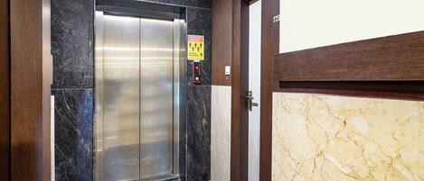 An elevator with a maximum capacity sign of 5 passengers, a door with a number 60, and a marble floor.