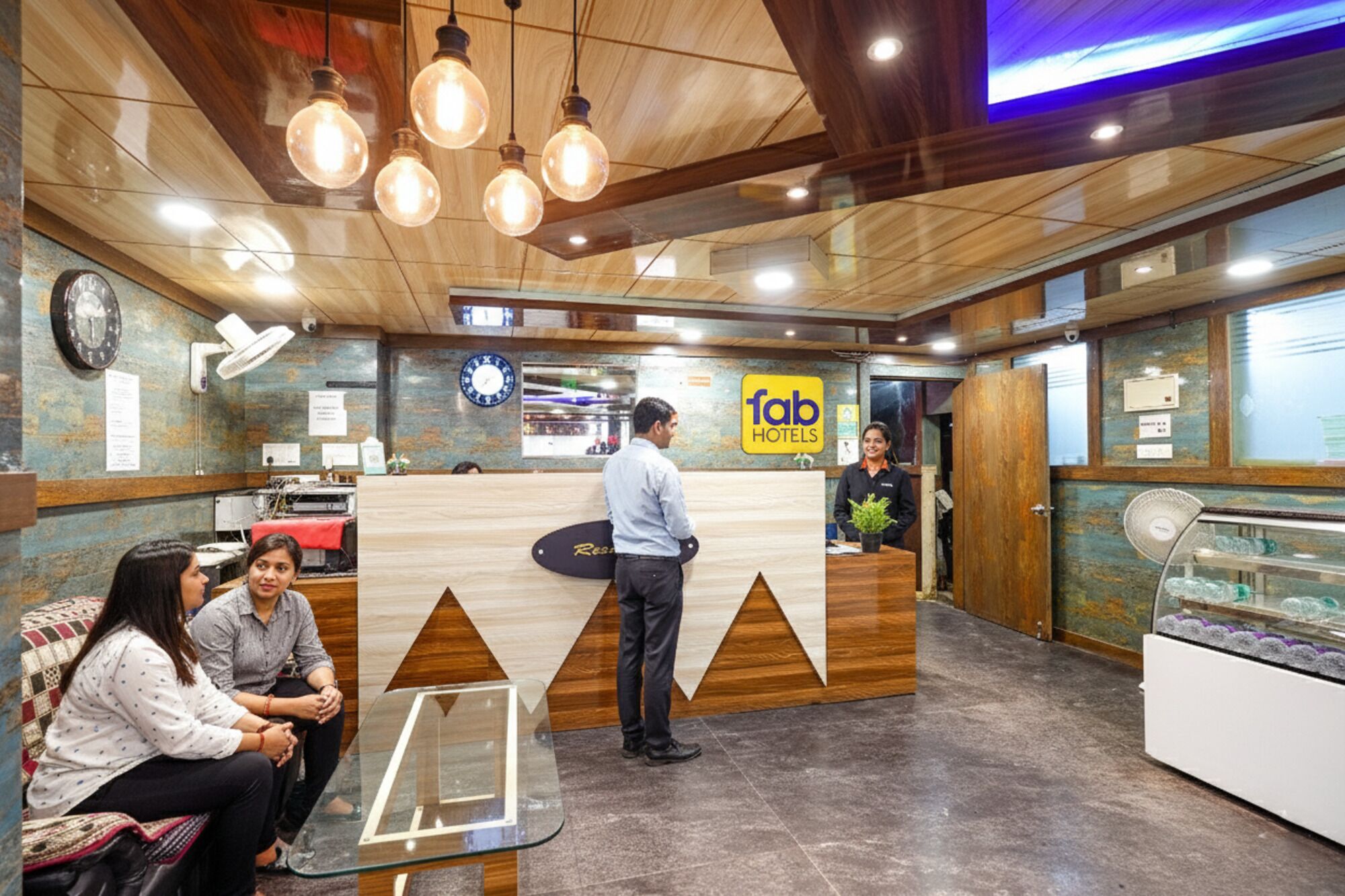 A hotel reception area with a wooden reception desk, a clock, and a sign for 'fab hotels'.