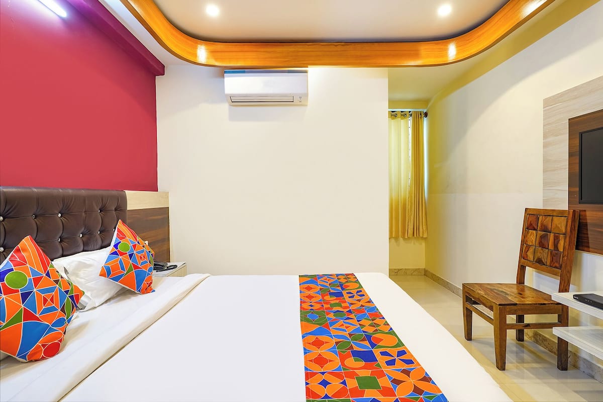 Una habitación de hotel con cama, cabecera de madera, una mesita, una silla y televisor.