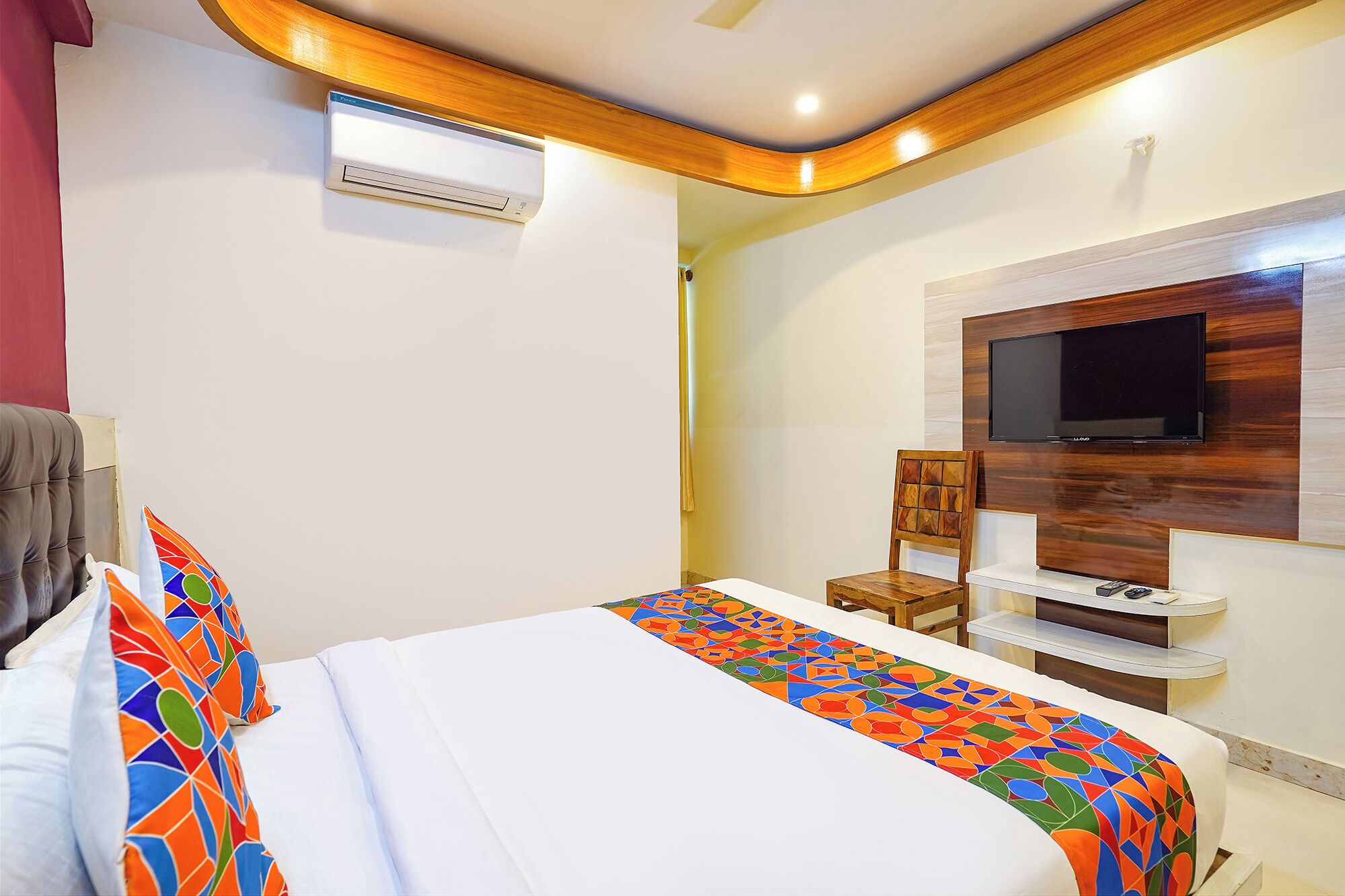 Una camera d'albergo con un letto, una TV a muro e un condizionatore d'aria a soffitto.