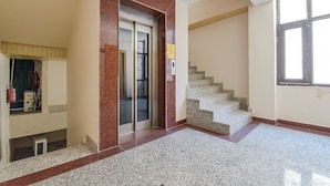 A spacious lobby with a marble floor, a staircase, and a fire extinguisher.