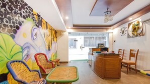 A room with wicker chairs and a small table, a wooden cabinet, and a wall with a clock and artwork.