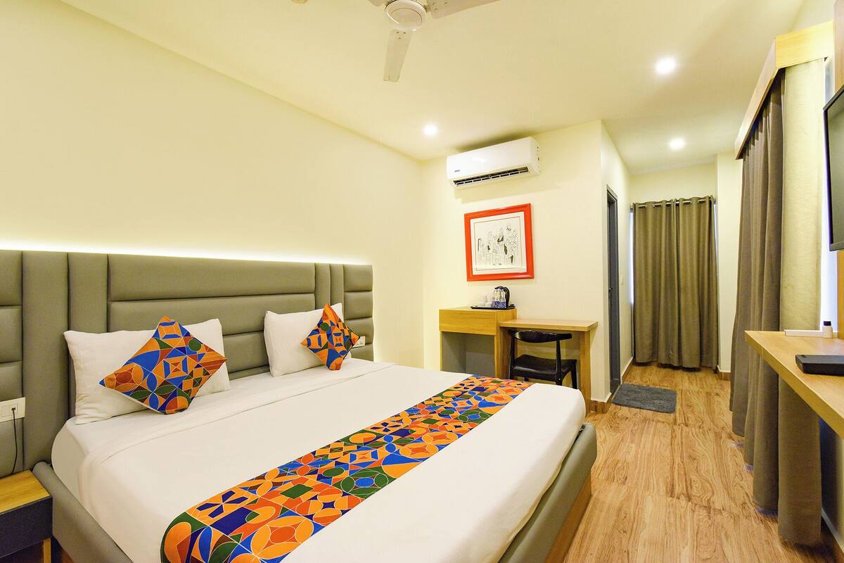 A hotel room with a bed, a desk, a chair, an air conditioning unit, and a shower area.