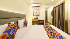 A hotel room with a bed, a desk, and a chair. There is a window with curtains, an air conditioning unit, and a framed picture on the wall. - Fabhotel White Ridge (Hyderabad)