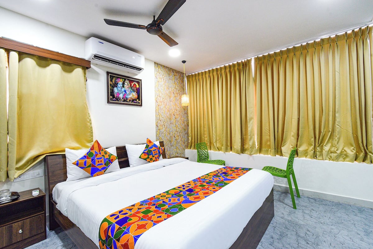 A hotel room with a bed, a nightstand, a green chair, a ceiling fan, and a window with curtains.